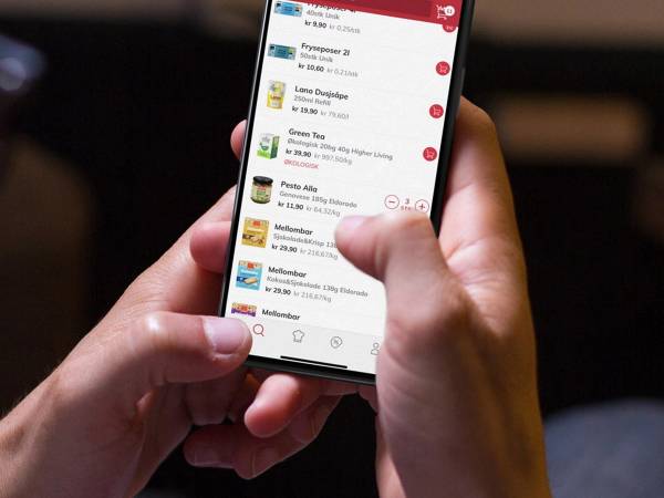 Person holder en mobil med en app som viser en liste over ulike produkter eller tjenester, med en rød toppmeny og ikoner nederst på skjermen.