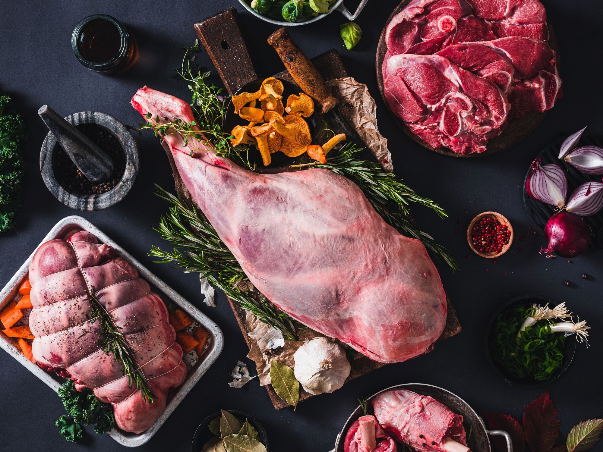 Ulike typer av lamme- og kjøttstykker på en svart bakgrunn med urter og krydder rundt.