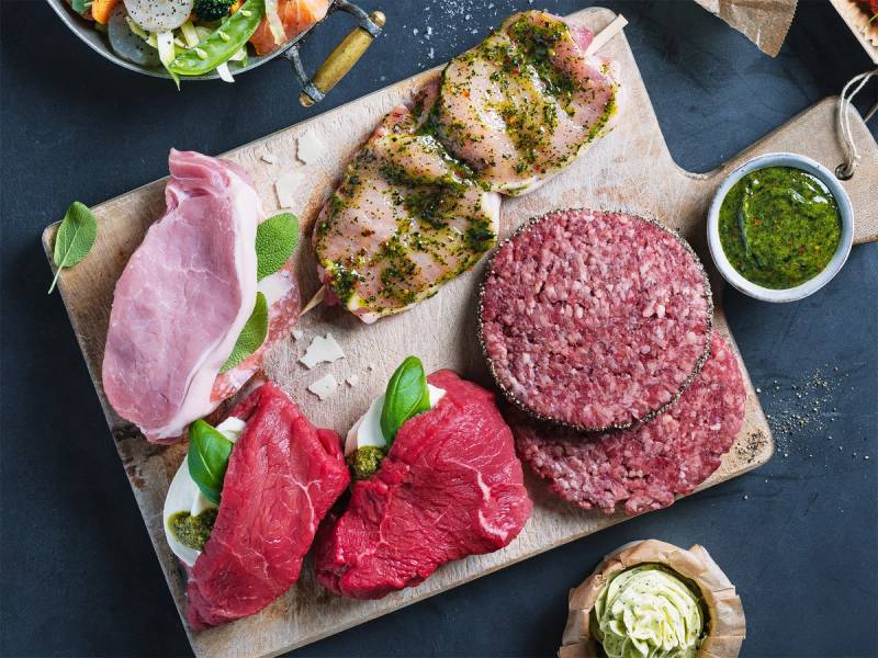 Ulike typer av kjøtt, inkludert biff og karbonadedeig, lagt ut på en skjærebrett med krydder og sauser ved siden av.