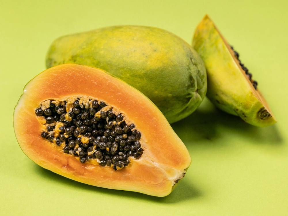 To papayaer, en hel og en halvert, med oransje kjøtt og svarte frø, på en grønn bakgrunn