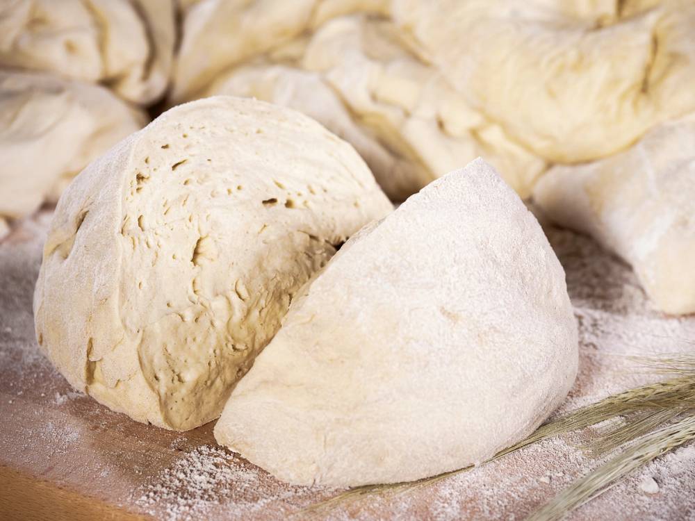 Bildet viser to baller av pizzadeig, en av dem er dekket med parmaskinke, klar til å bli brukt til pizza.