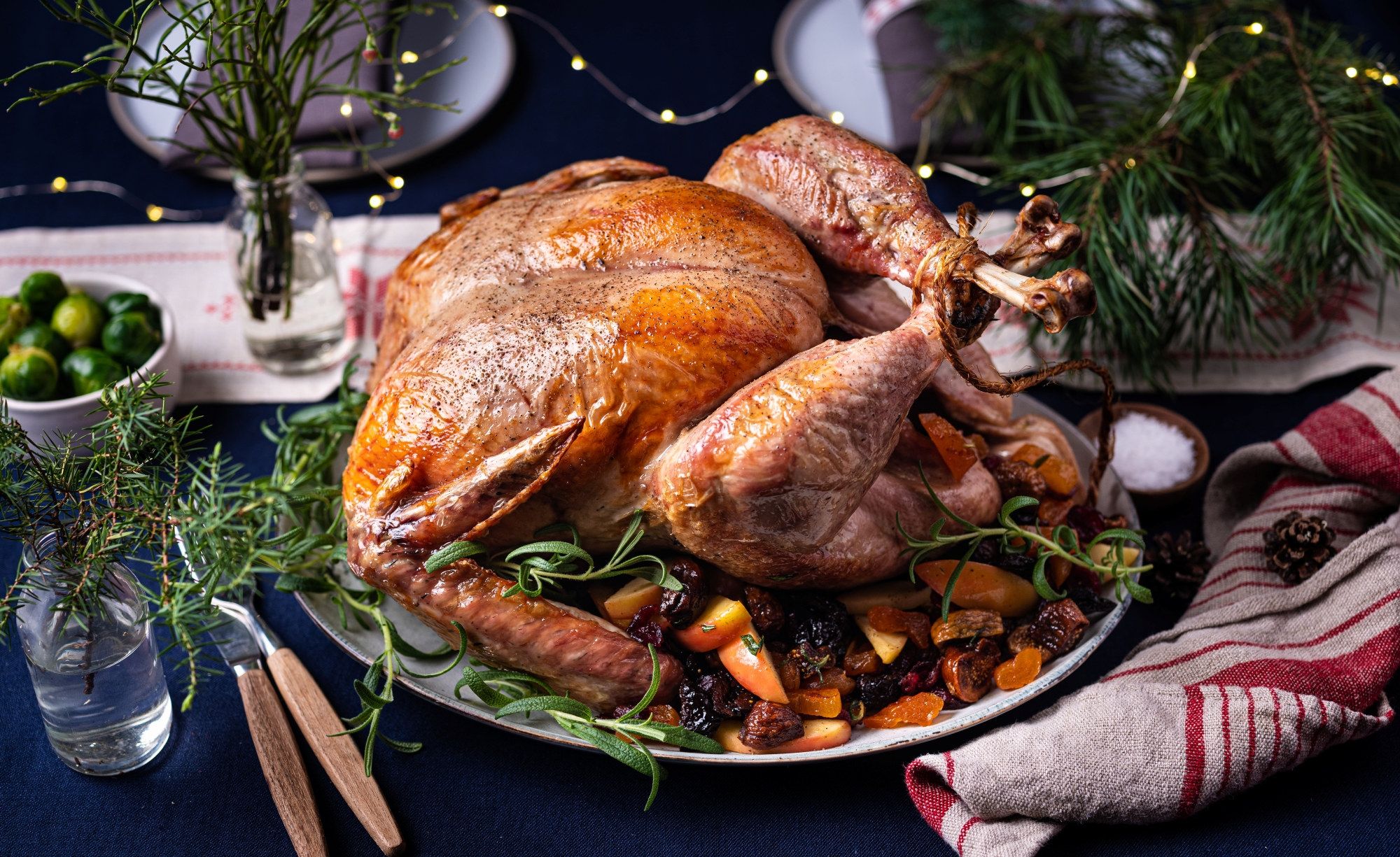 En stekt kalkun på et serveringsfat med grønnsaker og urter, omgitt av juledekorasjoner.