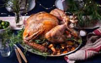 En stekt kalkun på et serveringsfat med grønnsaker og urter, omgitt av juledekorasjoner.