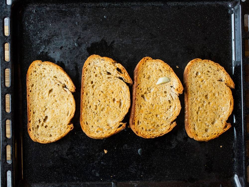 Fire skiver med brød på en stekeplate, klare til å bli toppet med pålegg.