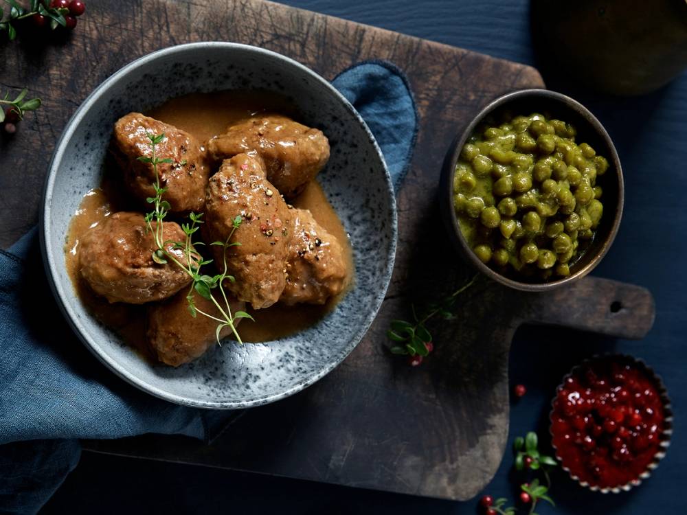 Kjøttkaker servert med brun saus og en liten skål med grønne erter på siden.