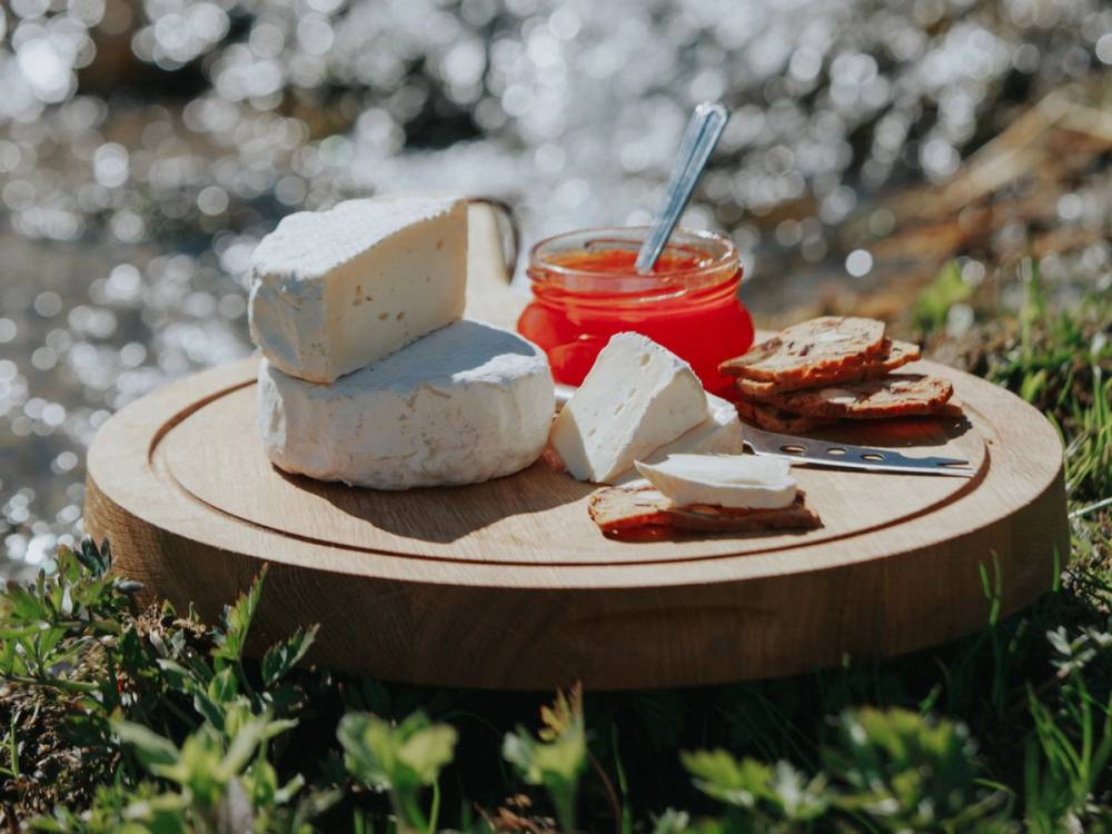 Camembertost med jordbærsyltetøy og spekeskinke på et rundt trefat utendørs.