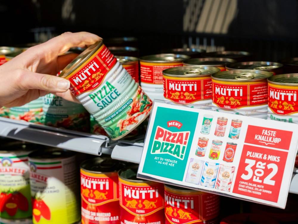 En person plasserer en boks med Mutti pizzasaus i en butikkhylle, omgitt av flere lignende produkter og reklame for pizza-tilbud.