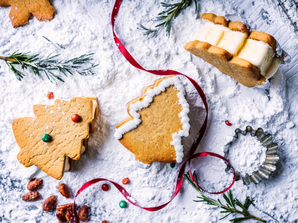 Pepperkaker i ulike former med julepynt og granbar på snøaktig bakgrunn.