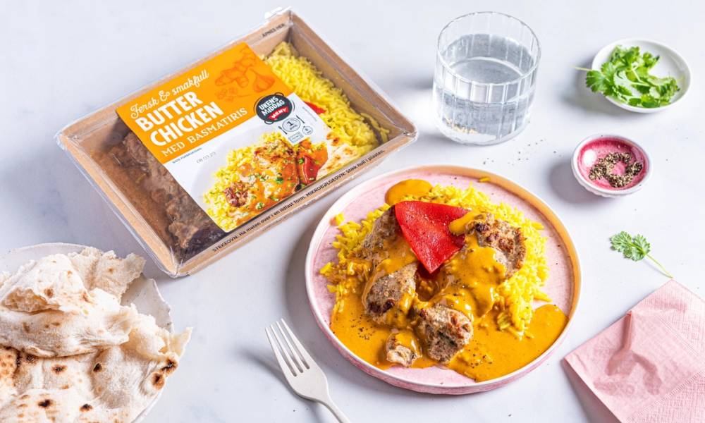 En tallerken med gul ris og kjøttboller i saus, omgitt av en pakke med ferdiglaget takeaway-mat, et glass vann og små skåler med krydder og urter.