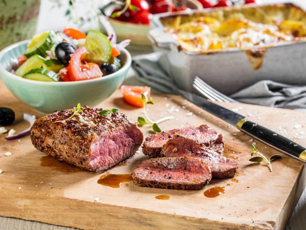 Sommermeny med grillet eller stekt fleskefilet og en frisk salat med grønnsaker og bær, samt en gratinert rett i en ildfast form i bakgrunnen.