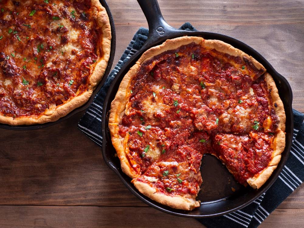 En stor, tykkbunns pizza med ost og kjøttdeig på en svart stekepanne, sett på et trebord.