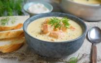 Fiskesuppe servert i en blå bolle med fersk dill på toppen, omgitt av brødskiver og tilbehør.