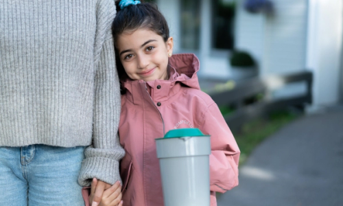 En person holder en innsamlingsbøtte mens en annen står ved siden av, utendørs på en gate eller fortau.