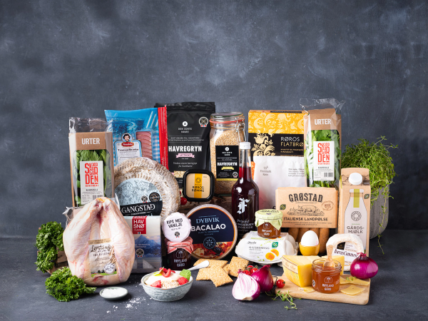 Et utvalg norske matvarer og produkter som ligger på en bordplate med en grå bakgrunn, inkludert kjøtt, egg, oster og krydder.