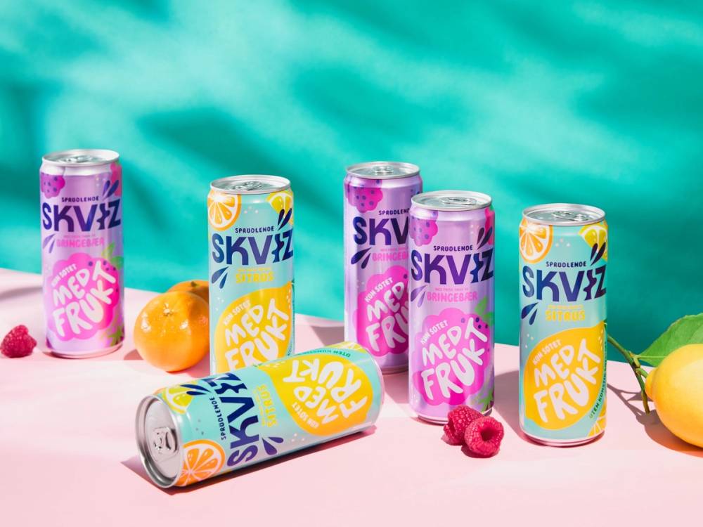 Flere bokser med SKVIZ-marksfrukt på et bord med frukt og blader rundt, mot en blå bakgrunn.