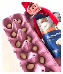 Egg i en rosa eggekartong med en julefigur som holder en yoghurtkartong ved siden av.