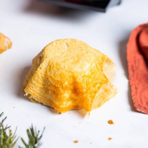 En krumkake som har blitt brettet og ser sprø ut, plassert på en hvit overflate med en liten del av en rød klut i bakgrunnen.