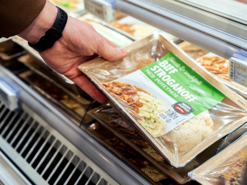 En hånd plukker opp en ferdig stroganoff-retter fra en kjøledisk i en butikk.