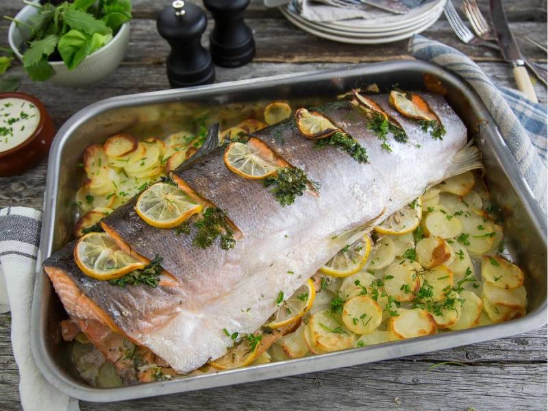 Helstekt laks med sitron- og urteskiver, servert på en stor ovnsform med potetskiver og grønnsaker.