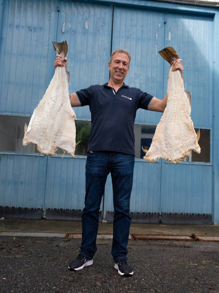 Person holder opp to store fisker, med blå bygning i bakgrunnen.