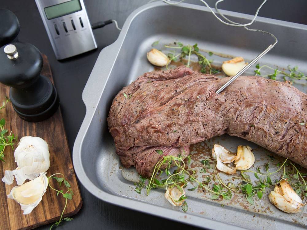 Indrefilet av okse i en ildfast form med hvitløk og urter, klar for steking eller steking, på en kjøkkenbenk.