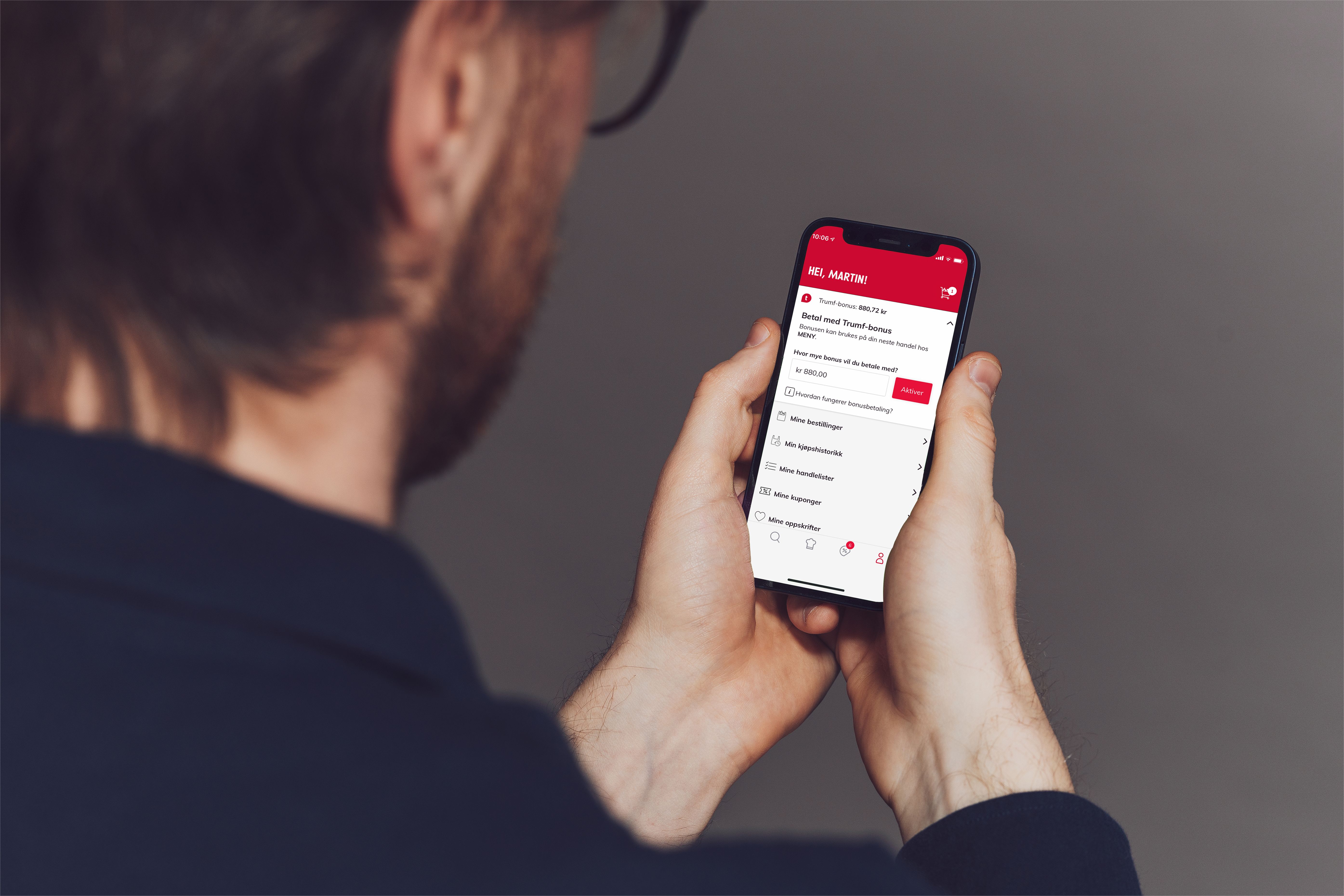 Person holder en smarttelefon som viser en betalingsapp med bonuspoeng, sett bakfra.