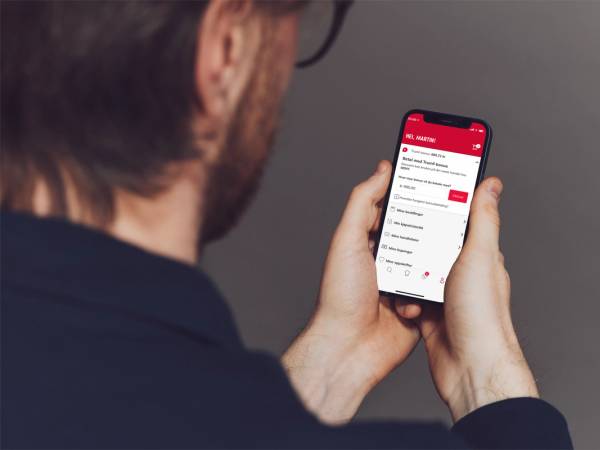 Person holder en smarttelefon som viser en betalingsapp med bonuspoeng, sett bakfra.