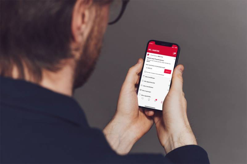 Person holder en smarttelefon som viser en betalingsapp med bonuspoeng, sett bakfra.