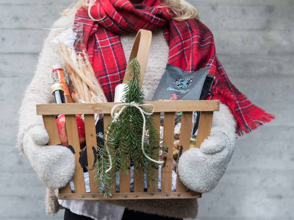 Person holder en kurv med hjemmelagde matgaver, iført rødt skjerf og vinterklær