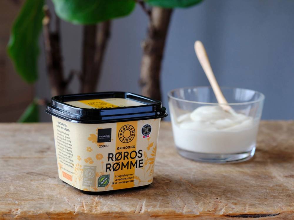 Økologisk Røros rømme fra Rørosmeieriet i en åpen plastboks og en skål med rømme og en skje ved siden av på et bord.