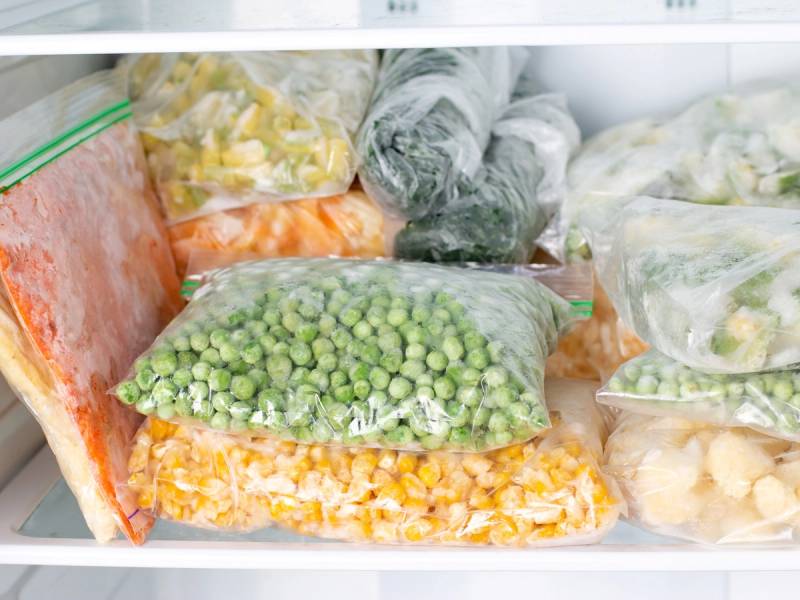 Frosne grønnsaker i plastposer i en fryser, inkludert erter, mais, spinat og brokkoli.