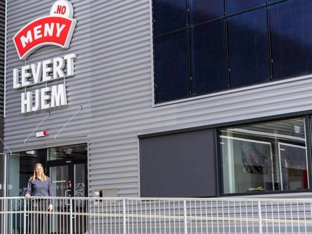 En kvinne står utenfor en butikk med et skilt som sier 'Meny levert hjem'.