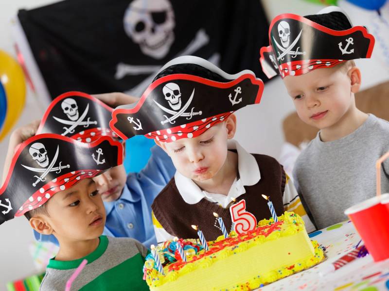 Barn feirer en bursdag med pirattema, med pirathatter og en bursdagskake på bordet.