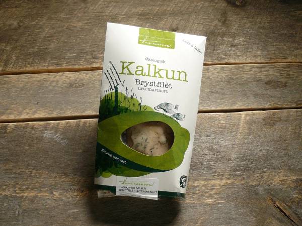 Pakke med kalkunbrystfilet på et trebord, med grønn og hvit emballasje og et vindu som viser kjøttet inni.