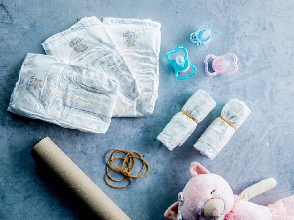 En samling bleier, smokker, bleieklemmer og en bleiekake med en bamse på et lyst bord.