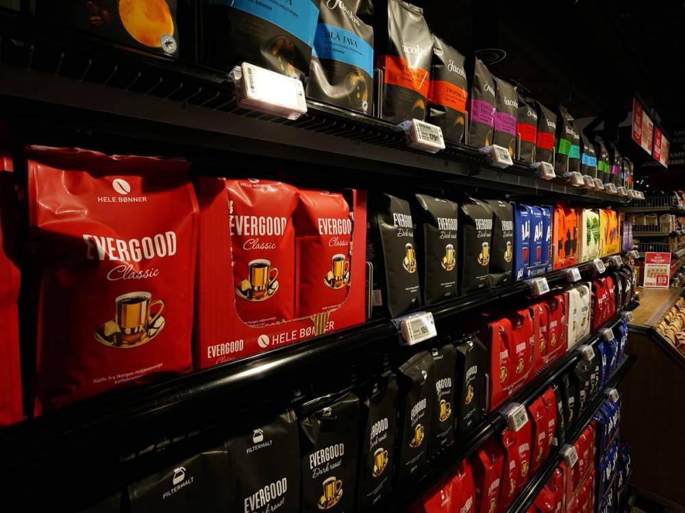 Hylla i en butikk med ulike typer kaffeposer i flere farger, inkludert rødt, svart og blått.