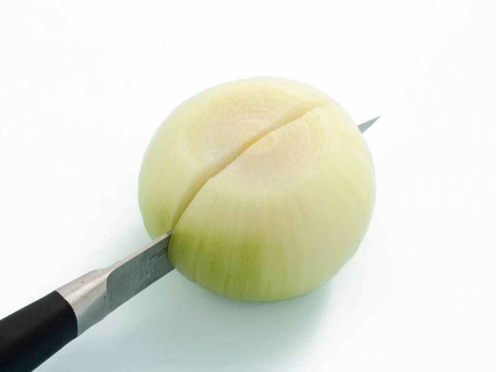 En hvit løk som er skåret i skiver med en kniv ved siden av.