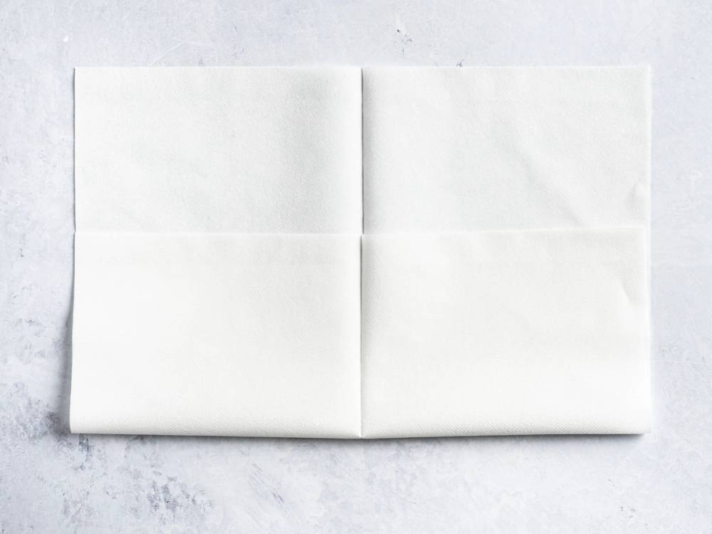 En hvit serviett brettet i en lommeform på et hvitt underlag.