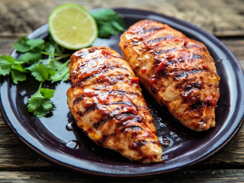 To grillet kyllingfileter med chili og marinade på en svart tallerken, pyntet med lime og koriander.