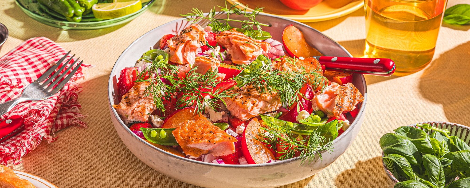 En fargerik sommer salat med tomater, agurk, urter og dressing i en stor bolle på et bord.