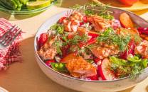 En fargerik sommer salat med tomater, agurk, urter og dressing i en stor bolle på et bord.