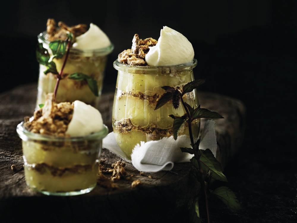 Tre små dessertglass med lagvis kake, krem og pynt, plassert på en mørk bakgrunn.