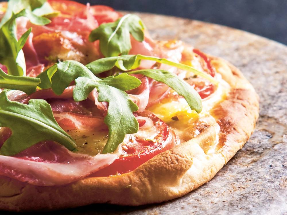 Pizza med skinke, tomater, ost og ruccola på en steinplate