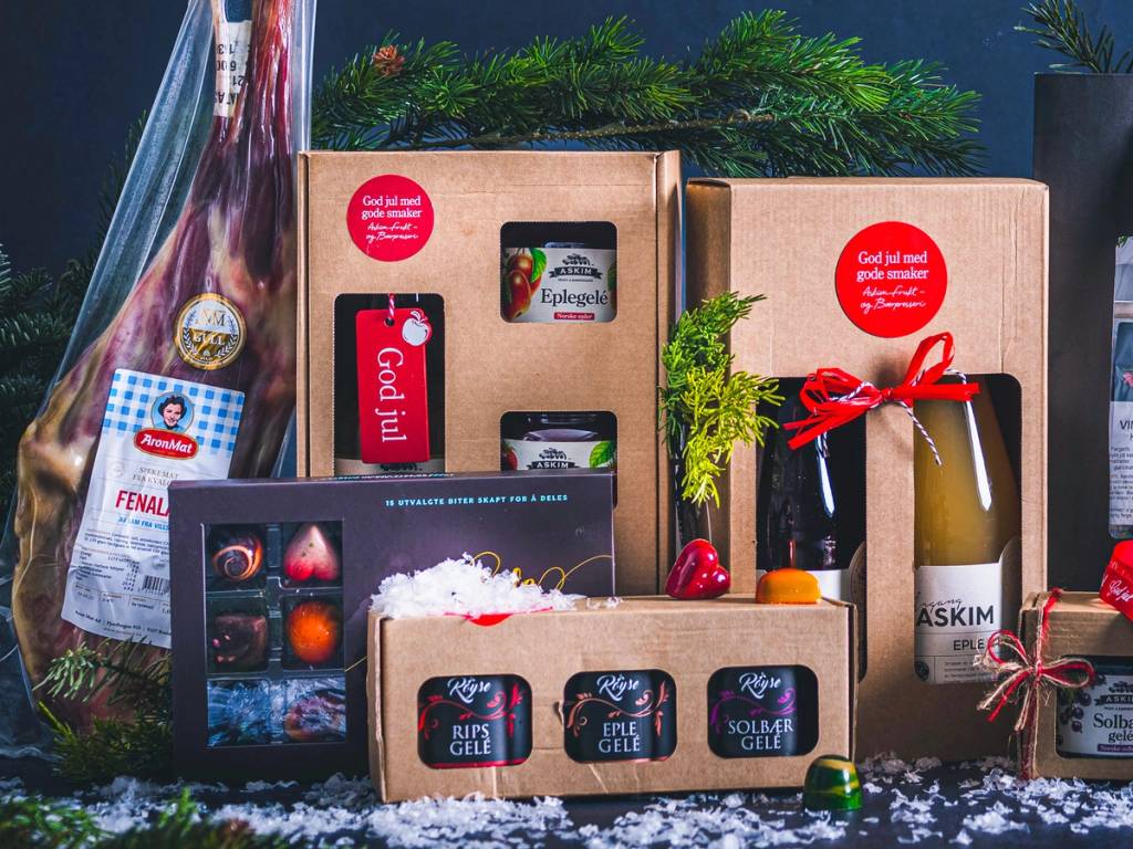 Ulike gaver og produkter pakket inn i esker og gavepapir, med julepynt og grønt dekorasjon rundt.