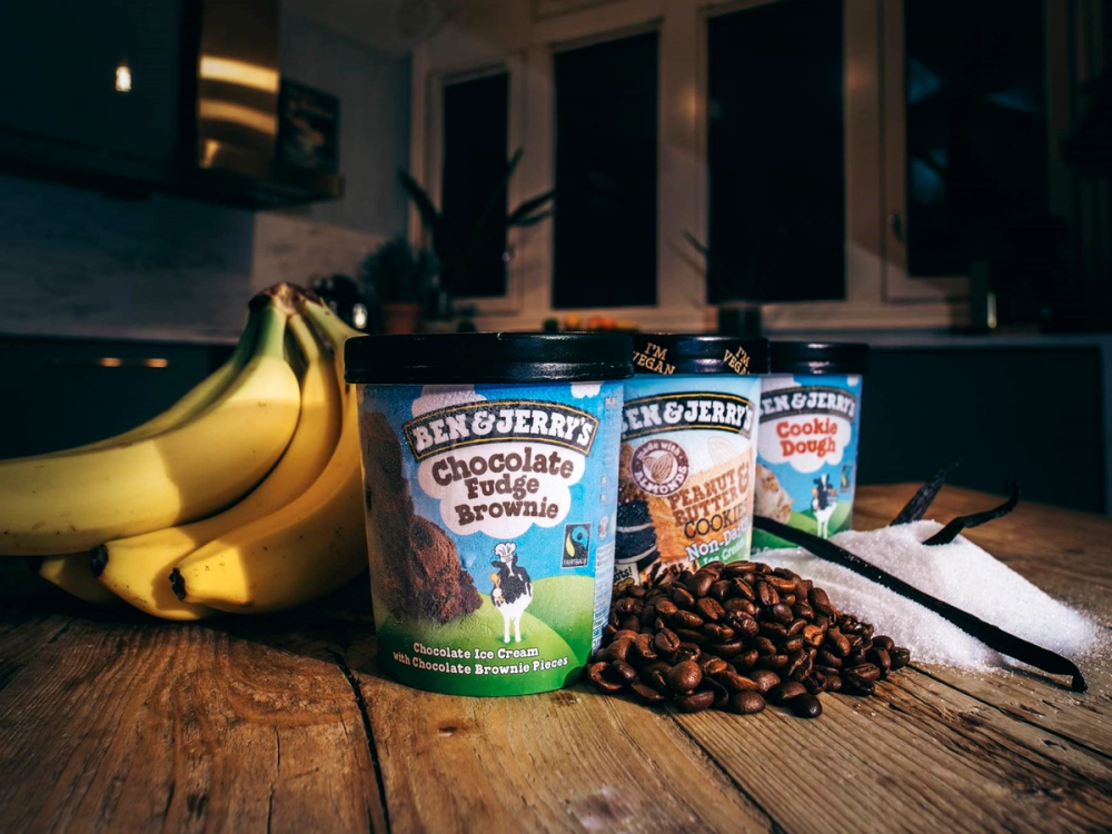 Tre iskremer med Fairtrade-merker, omgitt av kaffe og bananer på et kjøkkenbord.