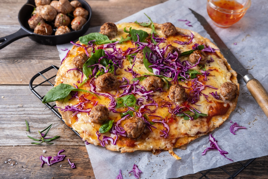 Medisterpølse på pizza med grønnsaker og ost, ser ut til å være en hjemmelaget pizza på et trebord.