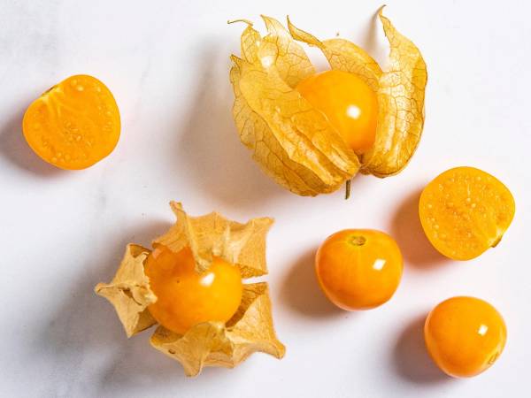 Physalis-frukt med sitt karakteristiske papiraktige omslag rundt den gule, runde frukten, plassert på en hvit bakgrunn.