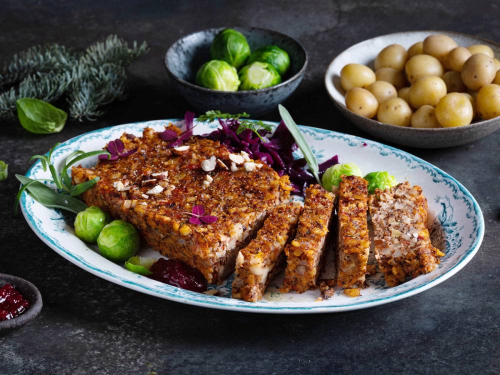 Nøttestek servert på et fat med grønnsaker og tilbehør, omgitt av poteter og grønnsaker i skåler.