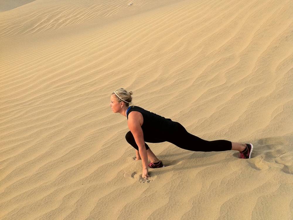 En person gjør en yogaøvelse på sanddyner i ørkenen
