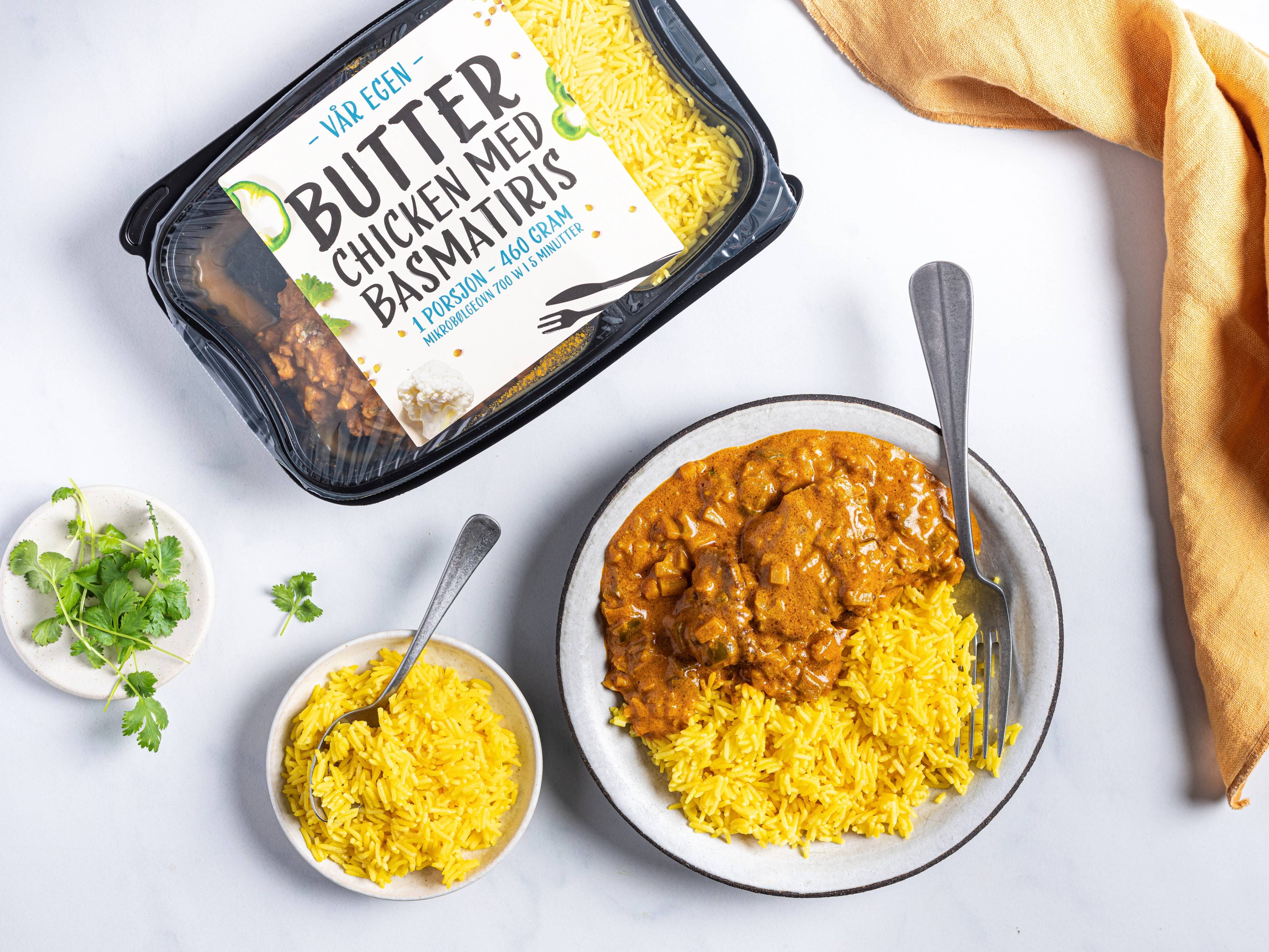 Bilde av en boks med butter chicken og ris, med en skje i hver tallerken, og en liten bolle med ekstra ris ved siden av.
